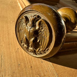 May include: A close-up of a wooden door knob with an eagle design. The knob is a dark brown color and the eagle is carved in detail.