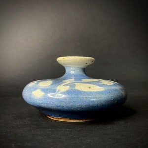 May include: A small, blue ceramic vase with a white glaze and a white design. The vase has a round base and a narrow neck.