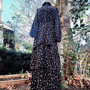 May include: A black tiered maxi dress with a floral print. The dress has a high neck and long sleeves.