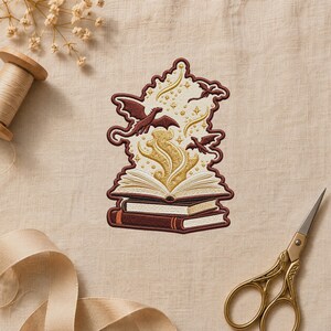 May include: An embroidered patch featuring a stack of two books with an open book on top. Golden magical energy swirls upward from the open pages, surrounded by two small dark red dragons and scattered gold stars, all outlined in dark red thread.