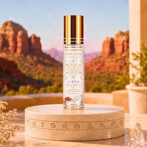 May include: A clear glass roller bottle with a gold cap, labeled Star Code Alchemy Libra Balance, featuring a gold geometric zodiac design, containing 10 ml or 0.34 fl oz of essential oil blend with visible crystals inside the bottle.