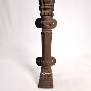 May include: A brown metal door handle shaped like a tower with intricate carvings. The handle is mounted on a white wall.