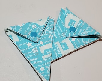 Op de afbeelding: Twee lichtblauwe stoffen muntportefeuilles met witte tekst en ontwerpen. De tekst omvat "Sew", "Make", "Create", "Just for you", "Do what you love", "Alive is a way of life", "Amend", "Dmade", "Maker", "Something new to", "Enjoy the process", "Being creative", "Do and mend", "Andmade", "In love", "Stitched", "Process", "New today", "Masters R".