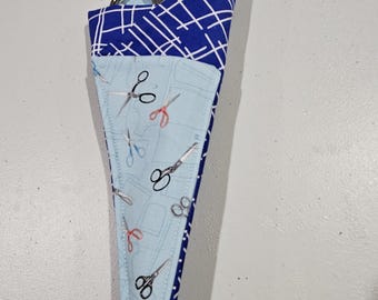 Op de afbeelding: Een blauwe en witte stoffen schaarhouder met een blauwe en witte gepatenteerde stoffen voering. De houder is gevuld met een zilveren schaar.