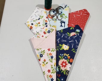 Op de afbeelding: Vijf stoffen schaarhoezen met bloemenpatronen. De hoezen zijn gemaakt van katoenen stof en hebben verschillende kleuren, waaronder roze, blauw, rood en wit. De hoezen zijn ontworpen om scharen en andere kleine naaiwerktuigen te bevatten.