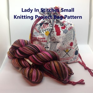 May include: A white knitting project bag with a colourful print of knitting-related phrases and images. The bag is made of fabric and has a drawstring closure. A skein of pink, brown and black yarn is in front of the bag.