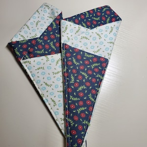 May include: Three fabric scraps sewn together to form a triangle. The fabric is white with a blue and green floral pattern, and navy blue with a red and green floral pattern.