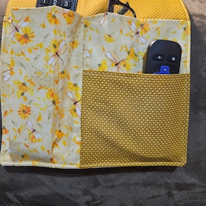 Sofa or chair arm caddy for remote control and other items including a book sleeve