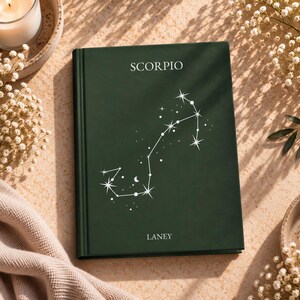 以下が含まれることがあります： 上部に白い文字でSCORPIO、下部にLANEYという名前が記されたダークグリーンのハードカバーノート。表紙の中央には、星のアクセントが施された蠍座の星座の白い線画イラストが描かれています。