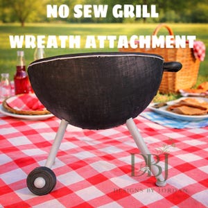 May include: A black, no-sew grill wreath attachment with white legs and a handle. The text "NO SEW GRILL WREATH ATTACHMENT" is displayed at the top of the image. The grill is set on a red and white checkered picnic blanket.