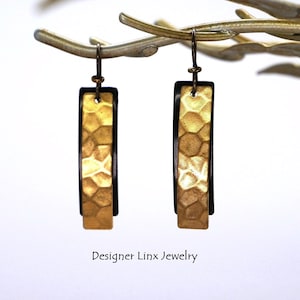 May include: Gold and black geometric earrings with a hammered texture. The earrings are rectangular in shape and have a simple design.