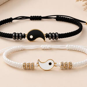 Puede incluir: Dos pulseras de cordón ajustable con dijes de yin-yang. La pulsera superior tiene un cordón negro con un dije de yin-yang negro y cuentas metálicas oscuras. La pulsera inferior tiene un cordón blanco con un dije de yin-yang blanco y cuentas con cristales.