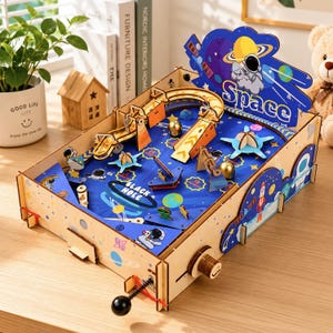 以下が含まれることがあります： 宇宙をテーマにした木製のピンボールゲーム。青いグラフィック、惑星、宇宙飛行士、そしてSpaceとBlack Holeの文字が描かれています。バネ式のプランジャー、金属製のボール、青いプレイフィールド上の様々な木製の障害物が含まれています。