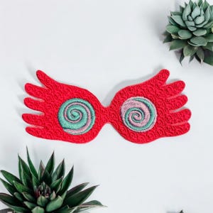 May include: Red embroidered patch of a pair of glasses with swirling green and pink lenses. The glasses are shaped like hands with outstretched fingers.