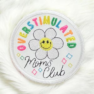 May include: White embroidered patch with a rainbow colored circle around the words "Overstimulated Moms Club". Inside the circle is a white daisy with a yellow smiley face.