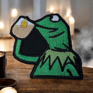 May include: Green embroidered patch of a frog drinking from a cup with the text "But that's none of my business"