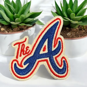 May include: A red, white, and blue embroidered patch with the letter "A" in a stylized font and the word "The" in front of it.