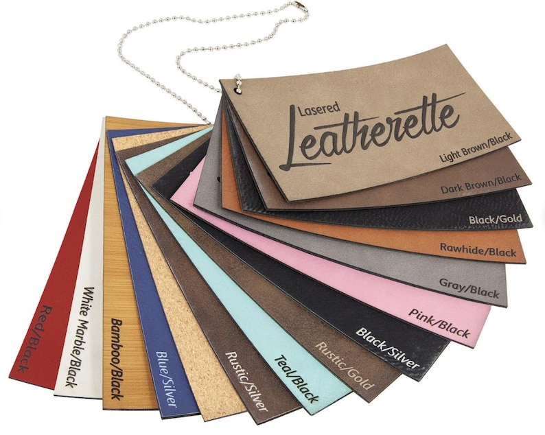 Op de afbeelding: Een waaier van kunstlederen kleurstalen, bevestigd aan een metalen kogelketting. De stalen tonen verschillende kleuren en texturen, waaronder rood, wit, blauw, bruin en zwart. De tekst "Lasered Leatherette" staat op het bovenste staal, met kleurnamen eronder.