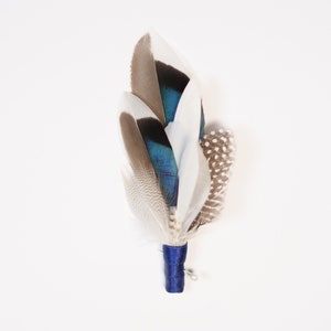 May include: A blue and white feather boutonniere with a navy blue ribbon and a pin.