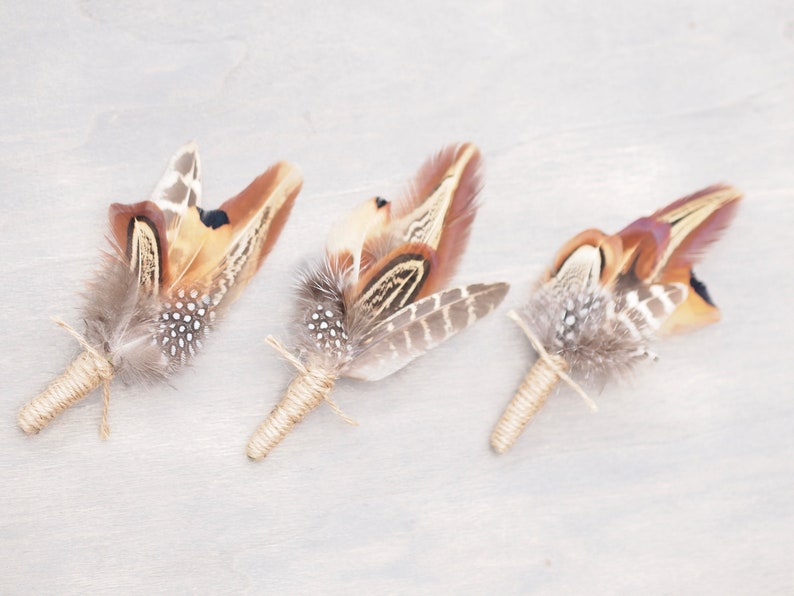 May include: Three brown and white pheasant feather boutonnieres tied with twine.