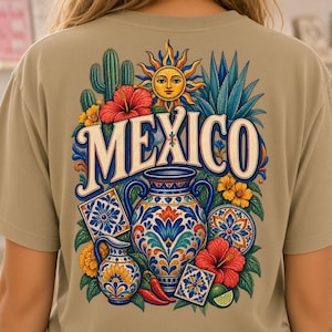 Può includere: Una t-shirt beige con una grafica colorata sul retro. Il design include la parola MEXICO in grandi lettere, circondata da un sole, un cactus, fiori di ibisco, peperoncini, un lime e due vasi in ceramica blu e bianchi decorati.