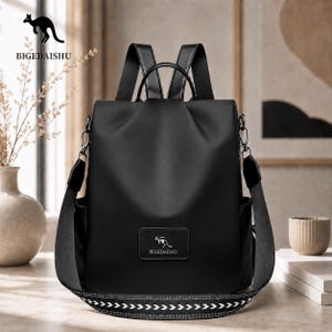 May include: A black backpack with a smooth finish, featuring a top handle, adjustable shoulder straps, and a rectangular patch on the front displaying the text BIGEDAISHU and a kangaroo logo. The base strap has a white geometric pattern.