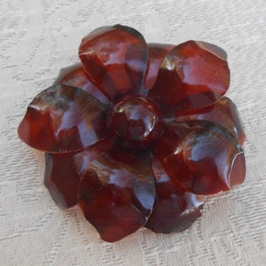 May include: A large, dark red, plastic flower brooch. The flower has five petals and a round center.