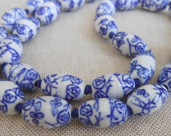 May include: A necklace featuring white, oval-shaped beads with a blue floral design. The beads are strung together with blue string. The necklace has a classic, elegant style, suitable for various occasions.