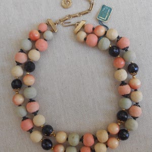 May include: A vintage double-strand necklace featuring a variety of colorful beads. The beads are in shades of pink, cream, black, and green, strung together with gold-tone metal accents. A small tag is attached to the necklace.