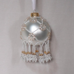 May include: A white glass Christmas ornament with a beaded design and gold accents. The ornament has a beaded fringe.