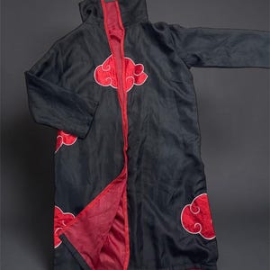 May include: A black long-sleeve cloak featuring a high collar and a red interior lining. The exterior is decorated with multiple red cloud-shaped appliques outlined in white. The garment is open at the front, revealing the red inner fabric.