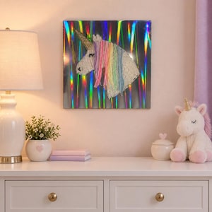 May include: A square wall art piece featuring a white unicorn head silhouette with a flowing rainbow-colored yarn mane, set against a reflective, holographic background with vertical light streaks in various vibrant colors.