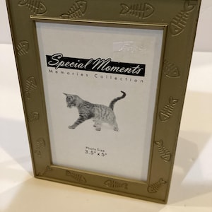 May include: Gold-colored picture frame with a fishbone design around the border. The frame has a white mat and says "Special Moments Memories Collection" and "Photo Size 3.5" x 5" at the bottom.