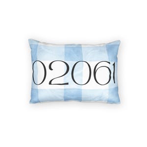 Peut inclure: Un coussin rectangulaire orné d'un motif à carreaux vichy bleu clair et blanc. Une bande blanche horizontale traverse le centre, affichant le texte numérique noir 02061 dans une police serif. Le coussin présente des coins arrondis.