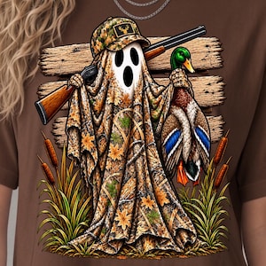 Peut inclure: Un t-shirt marron avec un motif représentant un fantôme portant un chapeau et une cape camouflage, tenant un fusil et un canard colvert. Le fond montre des planches en bois et des roseaux. Le texte Bamibo design Digital Download est visible.