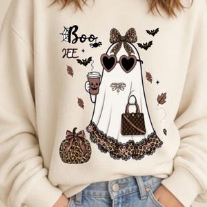 Peut inclure: Un sweat-shirt à col rond couleur crème arborant un motif de fantôme portant des lunettes de soleil en forme de cœur, un nœud à imprimé léopard et un ourlet léopard. Le fantôme tient un café et un sac à main, avec le texte Boo HEE et une citrouille.