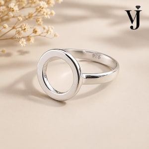 Puede incluir: Un anillo de plata pulida que presenta un diseño circular calado prominente en el centro. La banda interior del anillo está claramente marcada con el sello 925, lo que indica una composición de plata esterlina. La superficie es lisa y brillante.