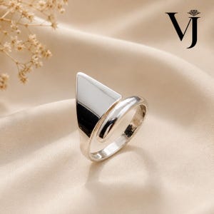 May include: A polished silver-toned ring featuring a prominent triangular-shaped flat top element. The band is smooth and rounded, connecting to the base of the triangle. The logo VJ with a small diamond icon is visible in the upper right corner.