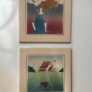 May include: Two square ceramic tiles featuring artistic illustrations. The top tile depicts a person in overalls holding a cluster of gold balloons against a red and dark blue sky. The bottom tile shows a house in a green field with a yellow sun.