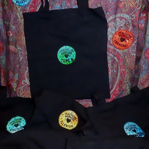 May include: A collection of black tote bags featuring circular patches with the text "HEALTHCARE WORKERS" and various artist names including Tape B, Excision, Illenium, John Summit, and Crankdat, each accented with a small heart and star icons.