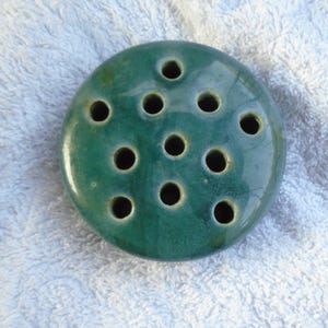 May include: A round, teal ceramic flower frog with 13 holes for arranging flowers.
