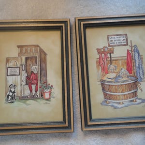 May include: Two framed watercolor prints. One depicts a person in a red outfit in an outhouse with a dog and text that reads "Welcome to the Outhouse Committee". The other shows two people in a wooden tub with text that reads "Save water, bathe with a friend".
