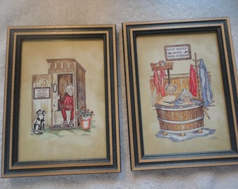 May include: Two framed watercolor prints. One depicts a person in a red outfit in an outhouse with a dog and text that reads "Welcome to the Outhouse Committee". The other shows two people in a wooden tub with text that reads "Save water, bathe with a friend".