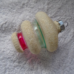 May include: A white glass Christmas ornament with a spiral design and a pink and green stripe. The ornament has a silver hanger.