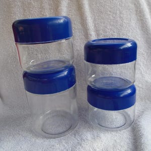 May include: Three glass storage jars with blue lids. The jars are stacked on top of each other. The jars are clear glass and the lids are a bright blue.