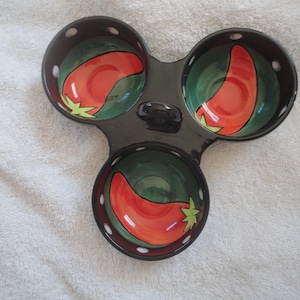 May include: A black ceramic serving dish with three individual bowls. Each bowl features a green and red chili pepper design.