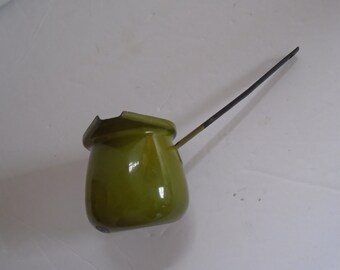 May include: A green enamelware pouring pot with a long black handle. The pot is slightly tilted to the side.
