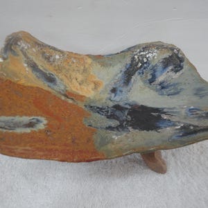 May include: A ceramic serving dish with an abstract design featuring shades of blue, brown, yellow, and white. The dish has three legs and is made in a rustic style.
