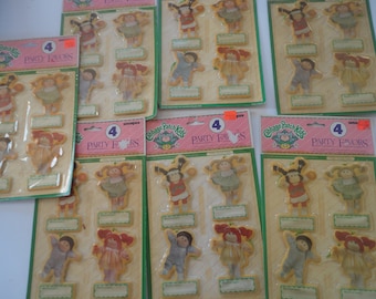 May include: Multiple packages of Cabbage Patch Kids party favors, each containing four individual doll-shaped stickers or tags with blank name labels. The packaging features pink and green headers with the text Party Favors and Cabbage Patch Kids.