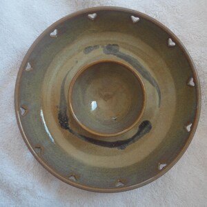 May include: A ceramic serving dish with a smaller bowl in the center. The dish has a light brown glaze with a darker brown swirl design. The edges of the dish have a scalloped design with heart-shaped cutouts.